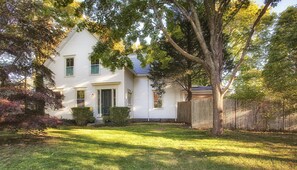 Situated in a lush environment, this traditional house offers a peaceful setting surrounded by a well-maintained lawn and a picket fence.