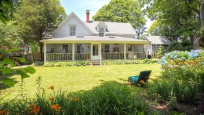 A two-story house with a porch, surrounded by a well-maintained lawn and garden. - Historic Captains House - Newly Renovated Primary Bathroom and Upgraded Kitchen (West Tisbury)