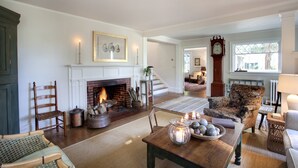 A cozy living room with a fireplace, comfortable seating, and a large clock on the wall. - Historic Captains House - Newly Renovated Primary Bathroom and Upgraded Kitchen (West Tisbury)