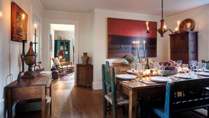 A dining area with a wooden table set for four, surrounded by chairs. A chandelier hangs above, and a large painting is on the wall. - Historic Captains House - Newly Renovated Primary Bathroom and Upgraded Kitchen (West Tisbury)