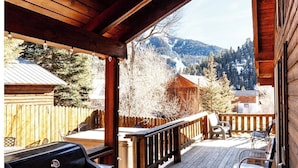 A wooden deck with a grill and chairs, overlooking a mountainous landscape. - Deer Mountain Lodge - High-End Home - In Town - Hot Tub - Free WiFi - Washer/Dry (Red River)