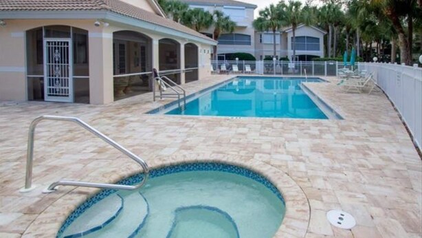 A swimming pool with a small hot tub, surrounded by a tiled deck and a white fence. - Centrally Located in Beautiful Naples (NAPLES)