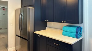 Une cuisine avec des meubles de couleur sombre, un réfrigérateur en acier inoxydable et un plan de travail sur lequel sont disposées des serviettes enroulées.