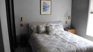 Ein Schlafzimmer mit einem großen Bett, einem Nachttisch, einer Wandlampe und einem gerahmten Bild.