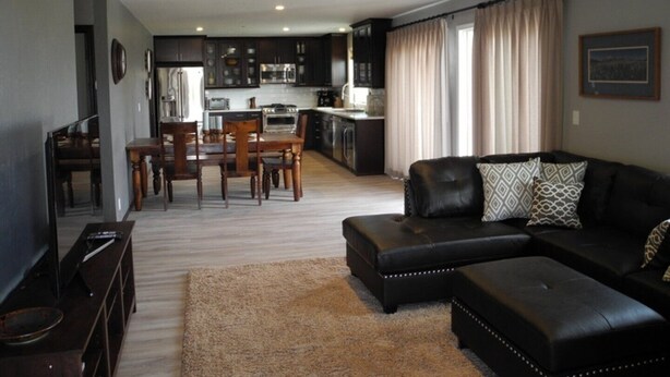 Ein modernes Wohnzimmer mit einer Ledersofa, einem Esstisch mit Stühlen und einer Küche im Hintergrund.
