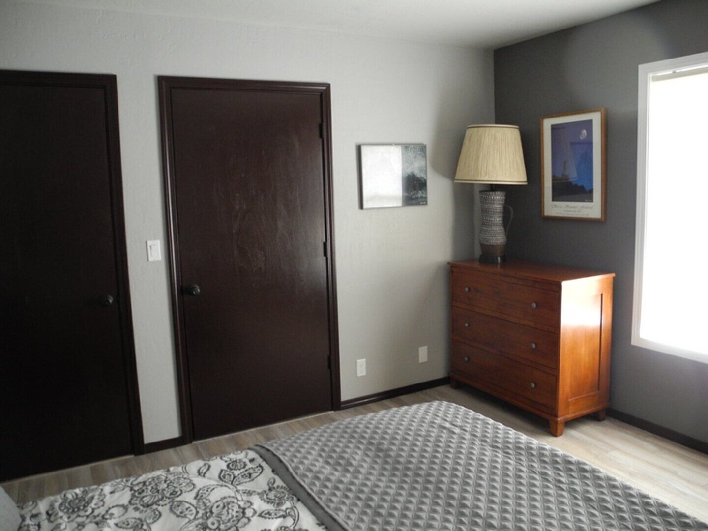 A bedroom with a bed, a dresser, two doors, and a window.
