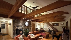 A spacious living room with a stone fireplace, wooden beams, a staircase, and a dog. - Spectacular waterfront home with panoramic views on 4 private acres ! (Harpswell)