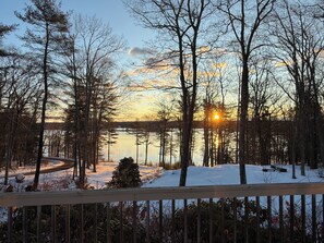 A winter landscape with a lake, trees, and a wooden deck.