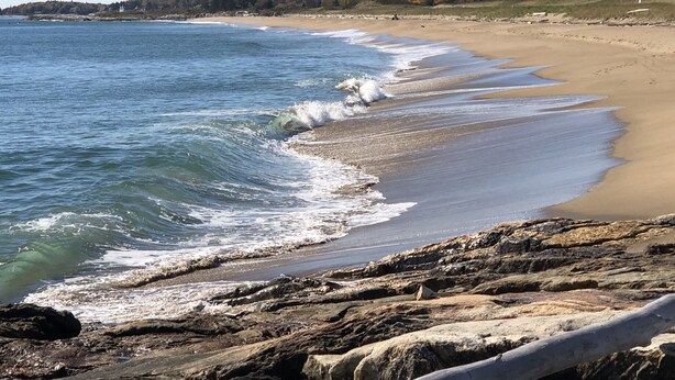 A beach with waves crashing onto the shore, rocky terrain, and a forested hill in the background. - Spectacular waterfront home with panoramic views on 4 private acres ! (Harpswell)