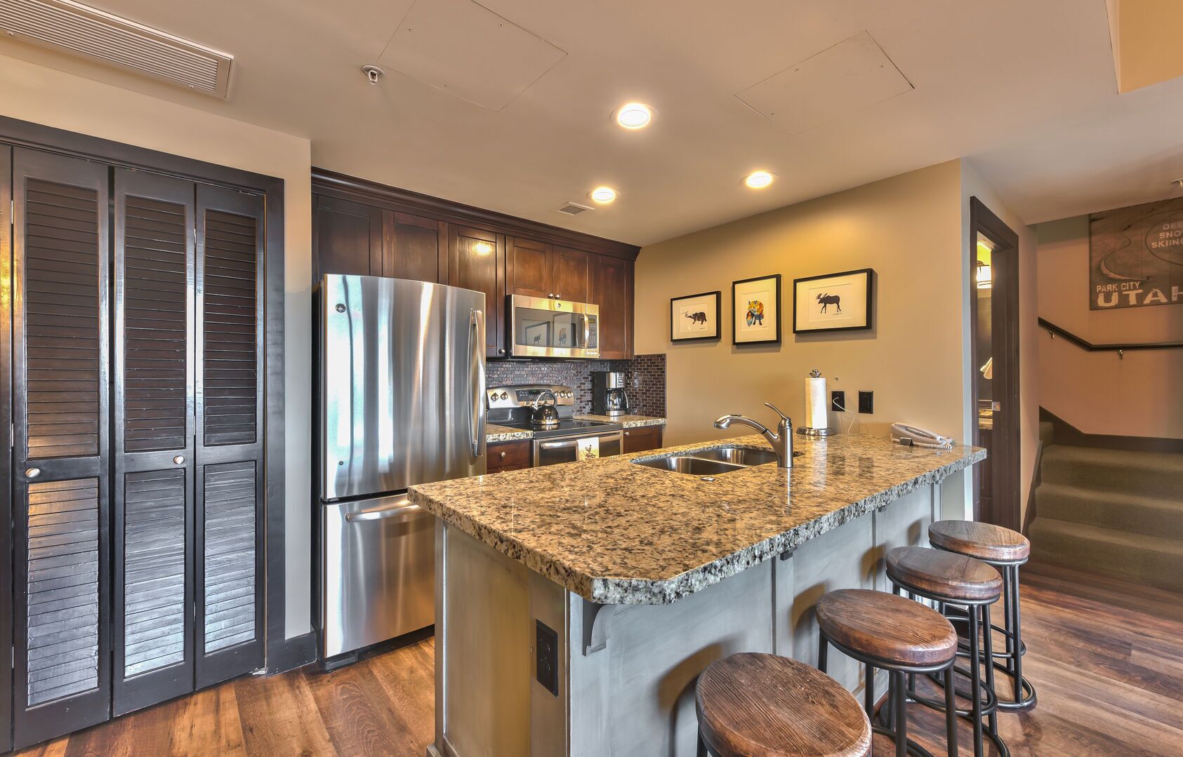 A modern kitchen with stainless steel appliances, a granite countertop, and wooden stools.
