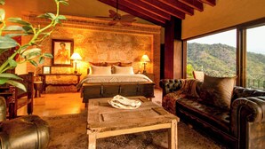 A bedroom with a large bed, a leather sofa, a coffee table, and a view of a mountainous landscape.