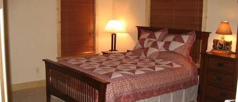 A bedroom with a wooden bed, two bedside tables with lamps, and a window with a wooden blind.