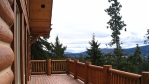 Um deck de madeira com guarda-corpo, com vista para uma paisagem montanhosa com árvores e céu nublado.