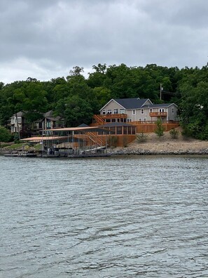 A waterfront property with a dock, a covered boat launch, and a multi-story house with a balcony.