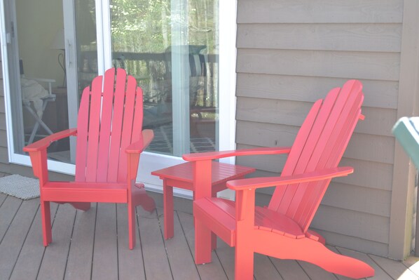 Dos sillas Adirondack rojas y una mesita en una terraza de madera.