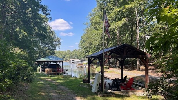 A covered picnic area with a gazebo, a small dock, and a boat on a lake, surrounded by trees. - Waterfront home on a quiet cove mid-lake! 4 kayaks, hot tub, and dog friendly!  (Mineral)