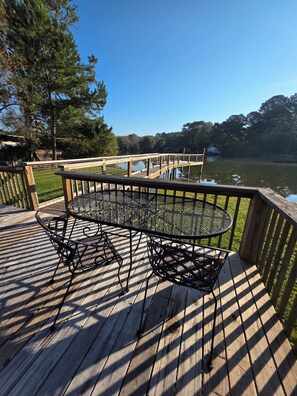 Un pontile in legno con tavolo e sedie in metallo, vista su uno specchio d'acqua e un molo.