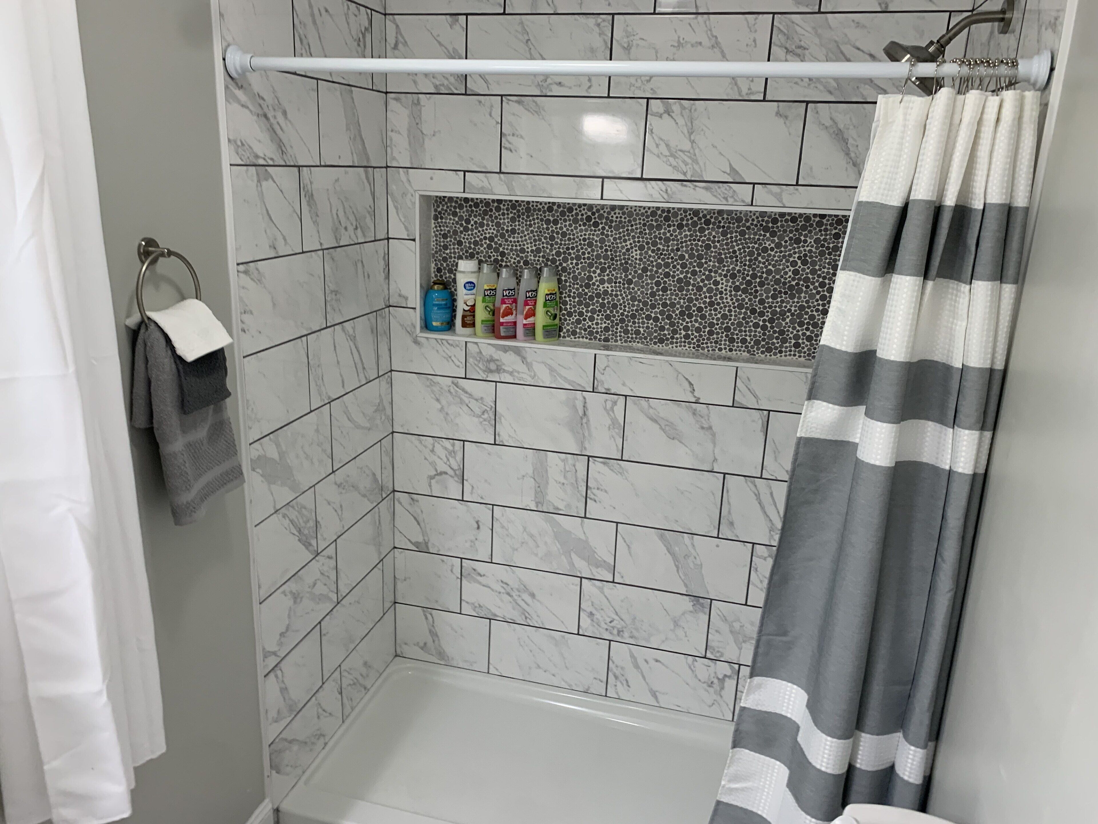 Une salle de bain avec une douche, des murs carrelés, un porte-serviettes et une étagère contenant des articles de toilette.