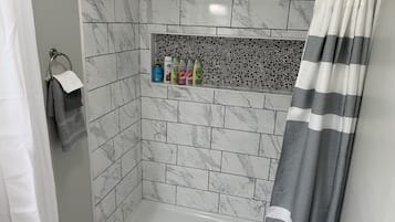 Une salle de bain avec une douche, des murs carrelés, un porte-serviettes et une étagère contenant des articles de toilette.