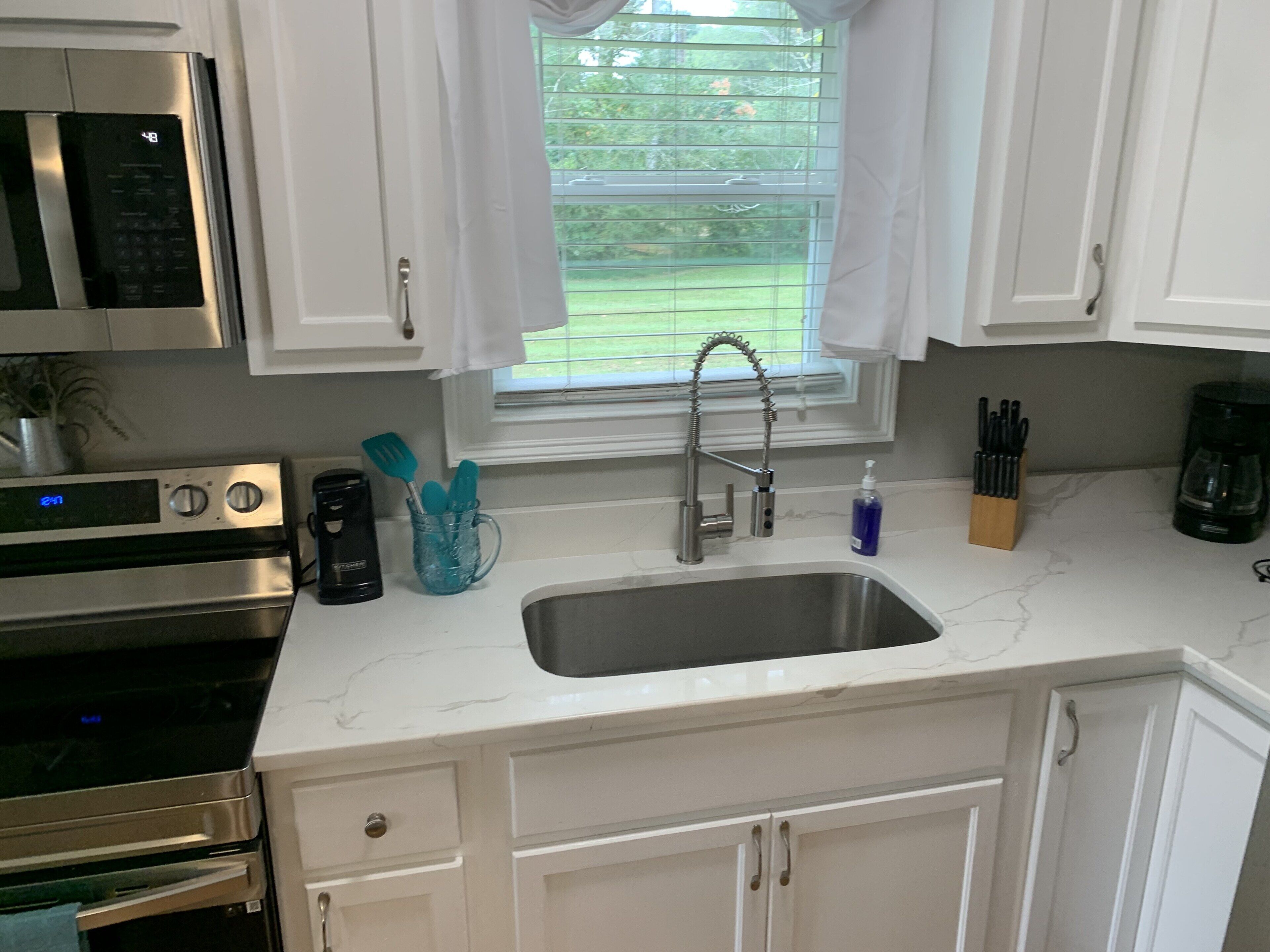 A kitchen with white cabinets, a stainless steel sink, a microwave, and a coffee maker.