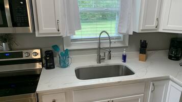 A kitchen with white cabinets, a stainless steel sink, a microwave, and a coffee maker.