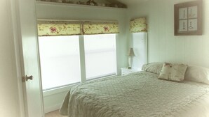 A bedroom with a bed, a nightstand, a lamp, and a window with blinds. - Natural High-Amazing Beach Getaway-Privacy, Easy Access, Kayaking, Boating (Cedar Island)