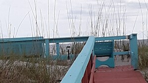 A wooden boardwalk with a light blue railing leading to a beach area. - Natural High-Amazing Beach Getaway-Privacy, Easy Access, Kayaking, Boating (Cedar Island)