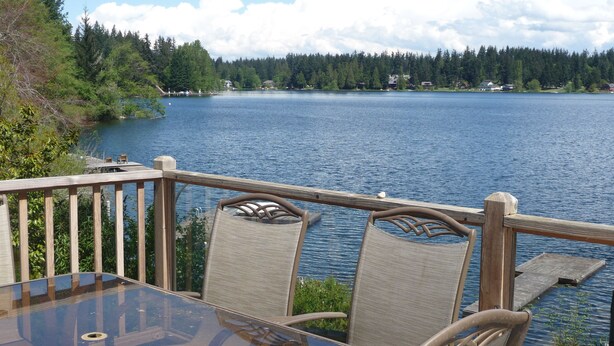 Un tavolo con piano in vetro e sedie in vimini su una terrazza che si affaccia su un lago.