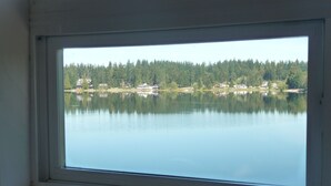 Una finestra che si affaccia su un lago tranquillo, circondato da una fitta foresta e diversi edifici.