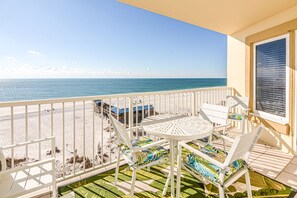 Ein Balkon mit Tisch und Stühlen, der auf einen Strand und das Meer blickt.