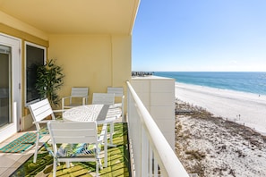 A balcony with a white table and chairs, a potted plant, and a view of the beach.