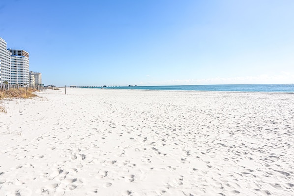 A beach with white sand and a pier in the distance.