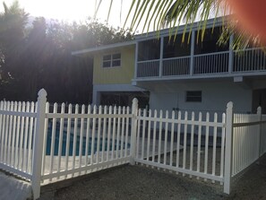 A two-story building with a white fence surrounding a swimming pool. - Canal Front Home With Pool And Hot Tub (Big Pine Key)