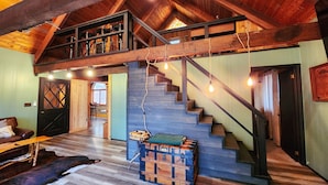 A spacious loft with a high ceiling, exposed wooden beams, a staircase with a wooden railing, and a cozy seating area with a leather couch and a rustic coffee table. - Secluded Pocono lodge, perfect for a weekend getaway with friends or family (East Stroudsburg)