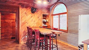 A rustic wooden interior with a dining table and chairs, a large arched window, and a wooden ceiling. - Secluded Pocono lodge, perfect for a weekend getaway with friends or family (East Stroudsburg)