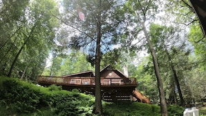 A cabin with a wooden deck and a chimney, surrounded by dense forest. - Secluded Pocono lodge, perfect for a weekend getaway with friends or family (East Stroudsburg)