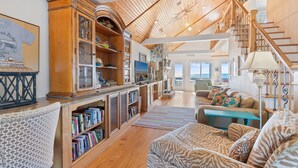 A spacious living area with a high ceiling, wooden staircase, and a cozy seating area with patterned cushions. - "Ocean Kiss" - Oceanfront Home, 6 Bedrooms / 4 Bathrooms (Holden Beach)