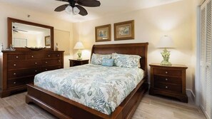 Ett sovrum med en stor säng, en byrå i trä, sängbord och en takfläkt.