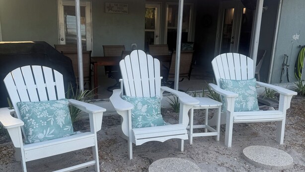 A covered outdoor seating area with three Adirondack chairs, each with a floral cushion, and a small table.