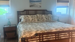 A bedroom with a wooden bed, a ceiling fan, a painting on the wall, and two windows with blinds.