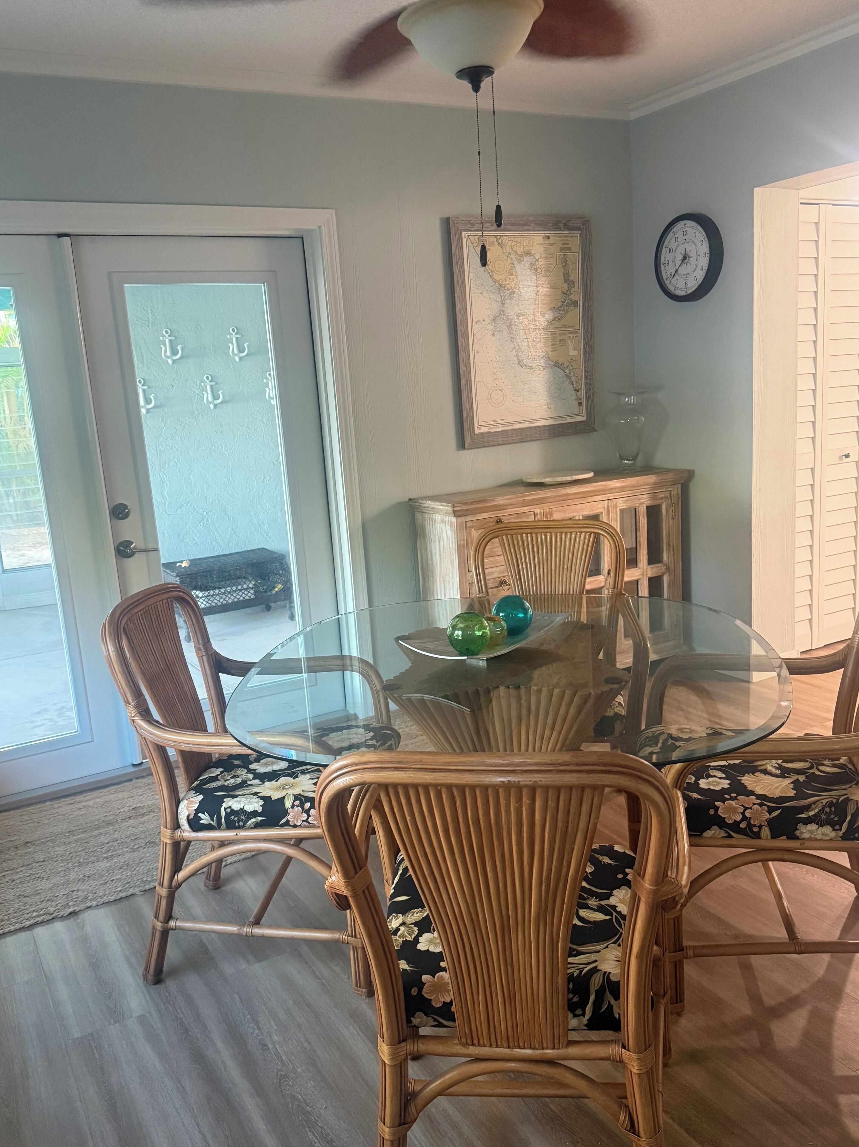 A dining area with a glass table, wicker chairs, and a wooden cabinet.