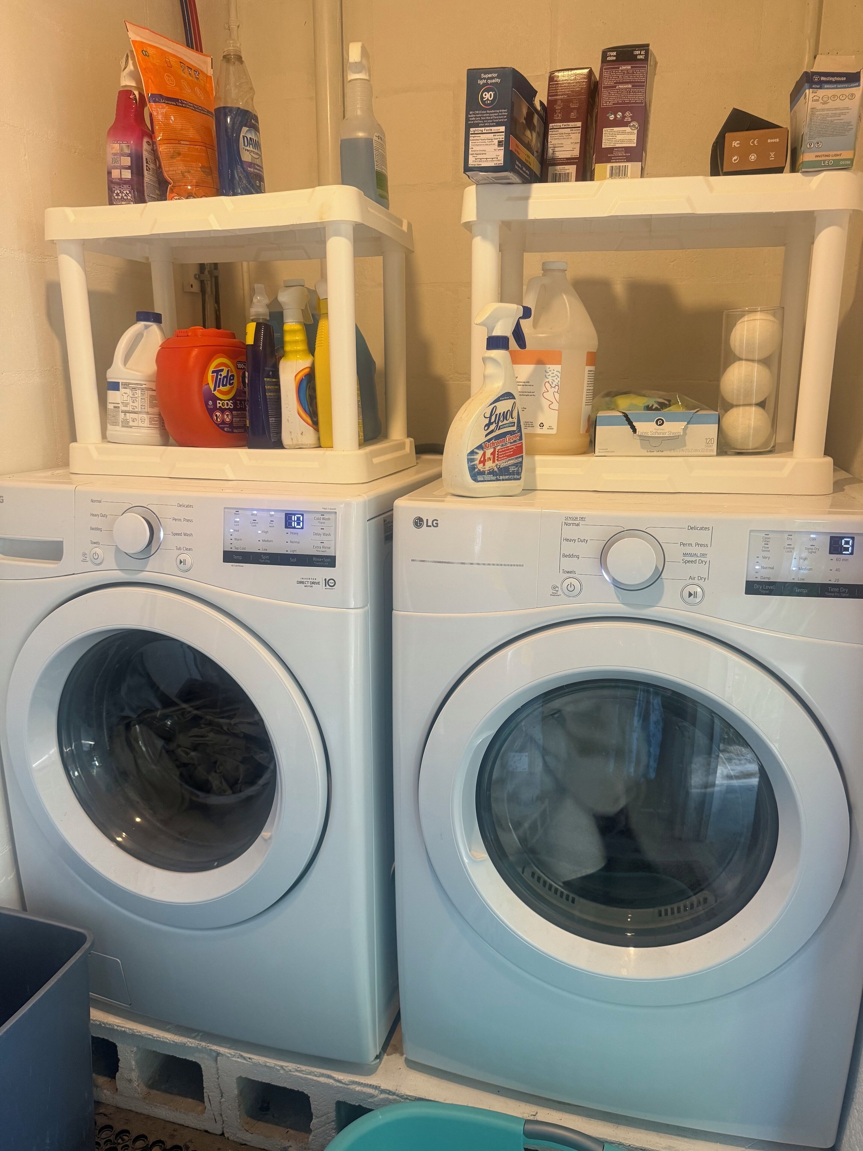 Two front-loading washing machines with detergent bottles and cleaning supplies on top.