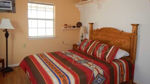 A bedroom with a wooden bed, a ceiling fan, a window, and a shelf with baskets. - Casa Tranquilla: Scenic Solar and Wind Powered Home (Alpine)