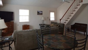 A living room with a sofa, a dining table, a TV, and two ceiling fans. - Casa Tranquilla: Scenic Solar and Wind Powered Home (Alpine)