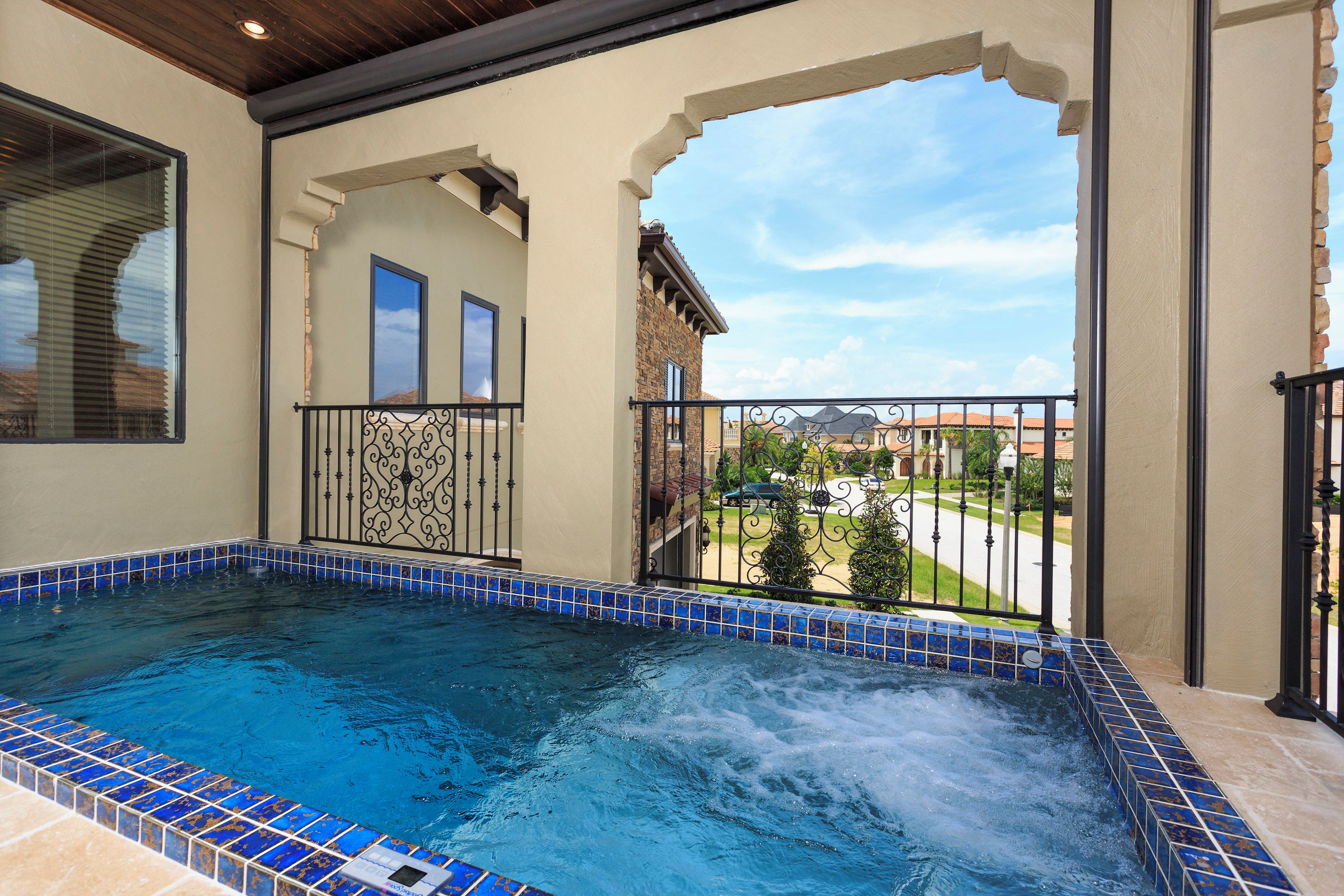 A hot tub with a tiled edge, a balcony with a railing, and a view of a residential area.