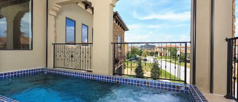 A hot tub with a tiled edge, a balcony with a railing, and a view of a residential area.