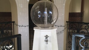 Een wit voetstuk met een bol erop, een waterfontein en een hekketting.