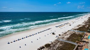 A beach with rows of blue lounge chairs and a lifeguard tower. - Oceanfront 2-bedroom condo in Panama City Beach, sleeps 8, ideal for families. (Panama City Beach)