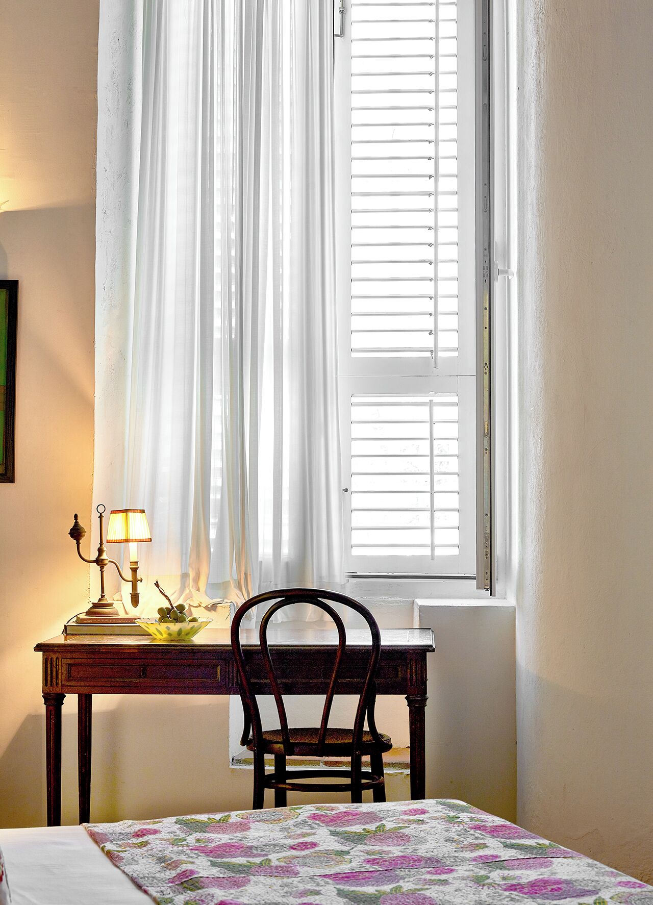 A room with a bed, a table with a lamp, a chair, and a window with blinds.