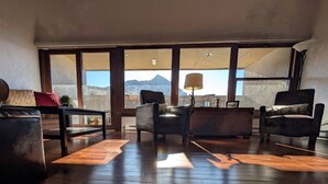 A spacious living room with a large window offering a mountain view, wooden flooring, and modern furniture.